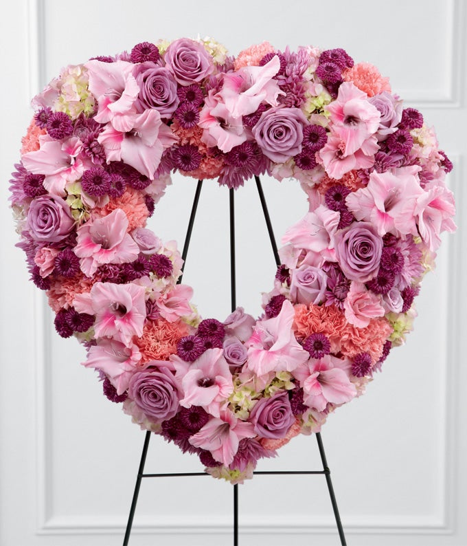 Heart shaped funeral standing spray with lavender roses pink carnations purple chrysanthemums pink gladiolus and hydrangea on easel stand