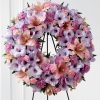 Pastel funeral wreath spray with periwinkle gladiolus pink lilies lavender chrysanthemums and mini carnations on easel stand