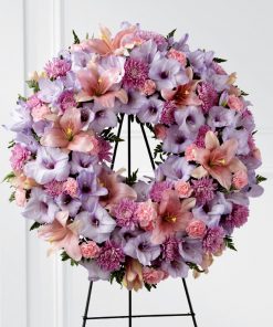 Pastel funeral wreath spray with periwinkle gladiolus pink lilies lavender chrysanthemums and mini carnations on easel stand