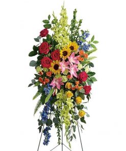 Vibrant remembrance standing spray with pink yellow orange roses lilies and blue delphinium